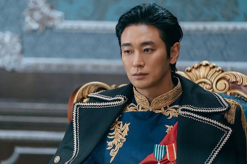 ator-do-dorama-the-wonder-fools-em-cena-dramatica-usando-uniforme-militar-azul-com-detalhes-dourados-e-medalhas-em-ambiente-palaciano